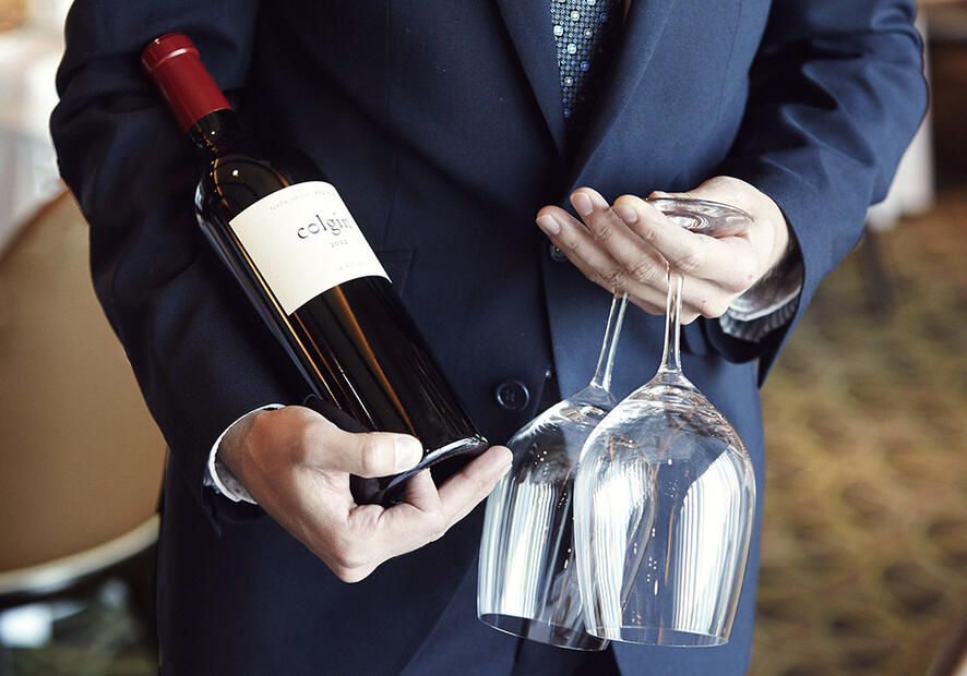 A sommelier carrying two glasses and a bottle of wine