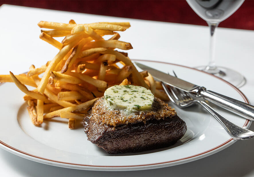Steak and fries on a plate with a glass of wine